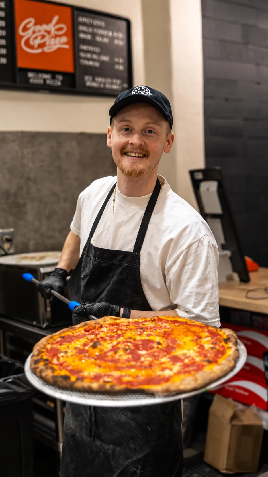 Good Pizza staff member holding a freshly baked pizza
